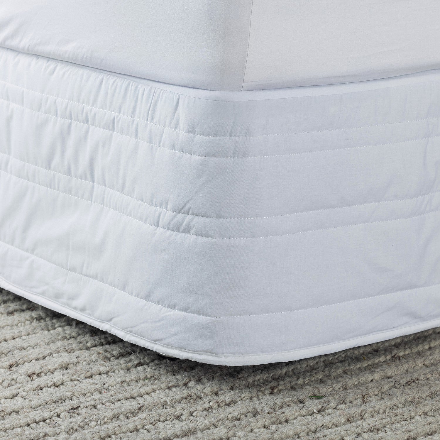 White quilted mattress protector on a bed with a carpeted floor.