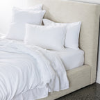 Neatly made bed with white bedding and pillows against a beige headboard.