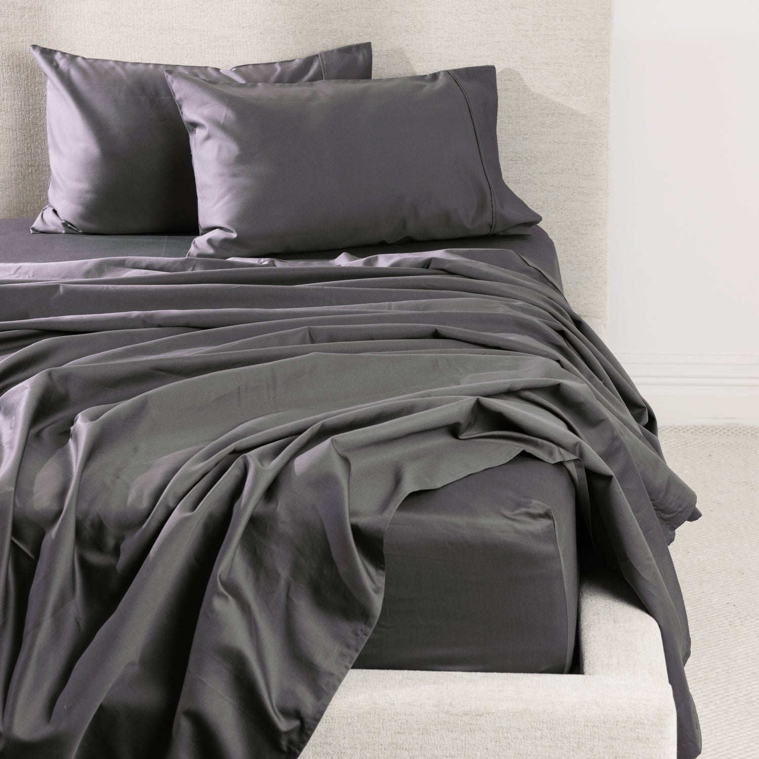 A luxurious charcoal sheet set is beautifully styled on a contemporary upholstered bed, showcasing its smooth, crisp finish and timeless elegance.