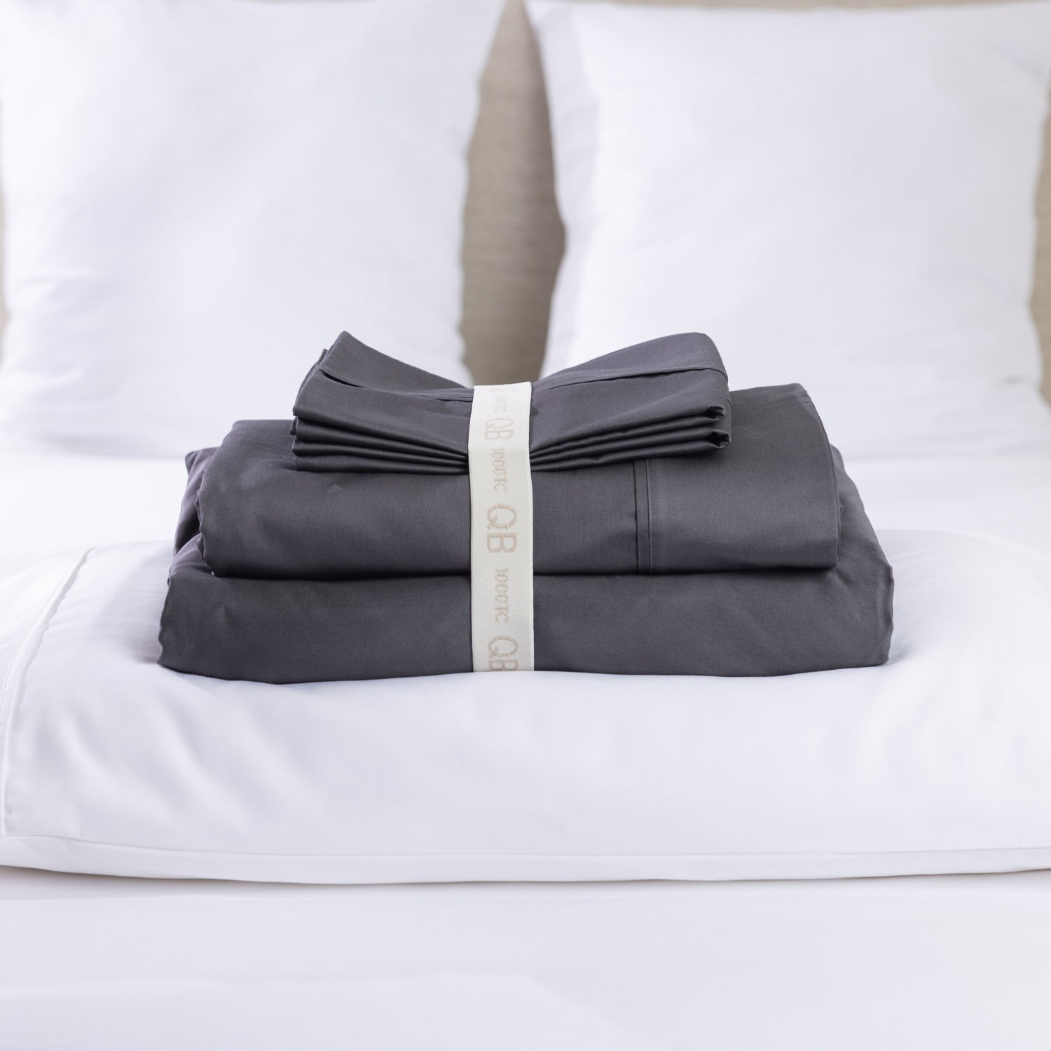 A premium charcoal sheet set is neatly folded and secured with a reusable branded storage band, beautifully displayed on a freshly made bed for a clean, luxurious look.