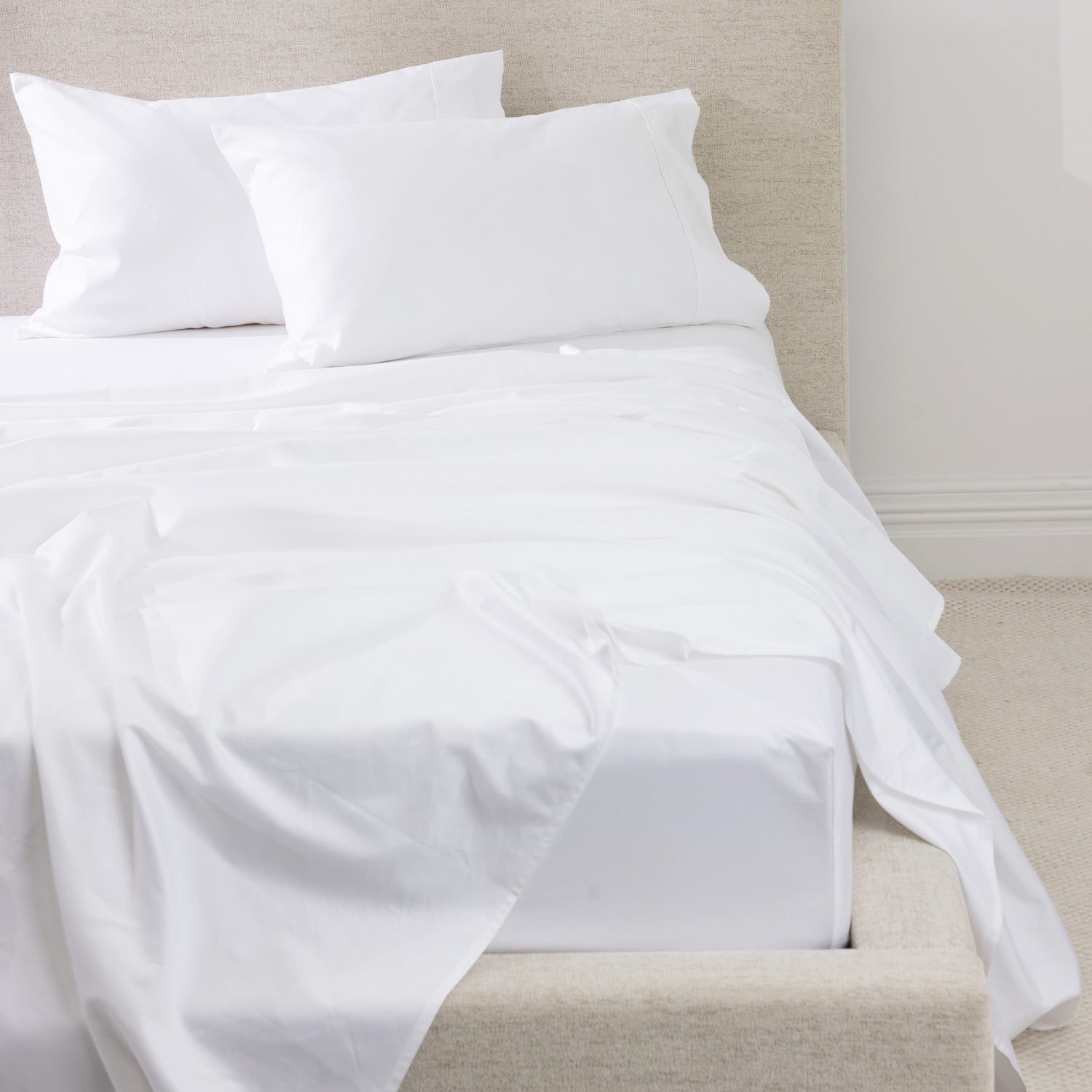 A luxurious white sheet set is beautifully styled on a contemporary upholstered bed, showcasing its smooth, crisp finish and timeless elegance.