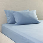 Light blue bedding set including a fitted sheet and two matching pillowcases on a bed against a textured beige headboard.