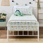 Dino Beach Party fitted sheet set styled on a white metal bed with coordinating printed pillowcase and a green dinosaur soft toy.