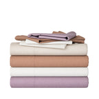 A stack of folded bedding sheets in muted neutral and pastel tones on a clean white background.