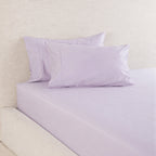 A Gracious Living Avery 750TC 100% Cotton Fitted Sheet in Dusky Mauve, neatly fitted over a mattress and styled with coordinating lavender-purple pillowcases against a neutral upholstered headboard.