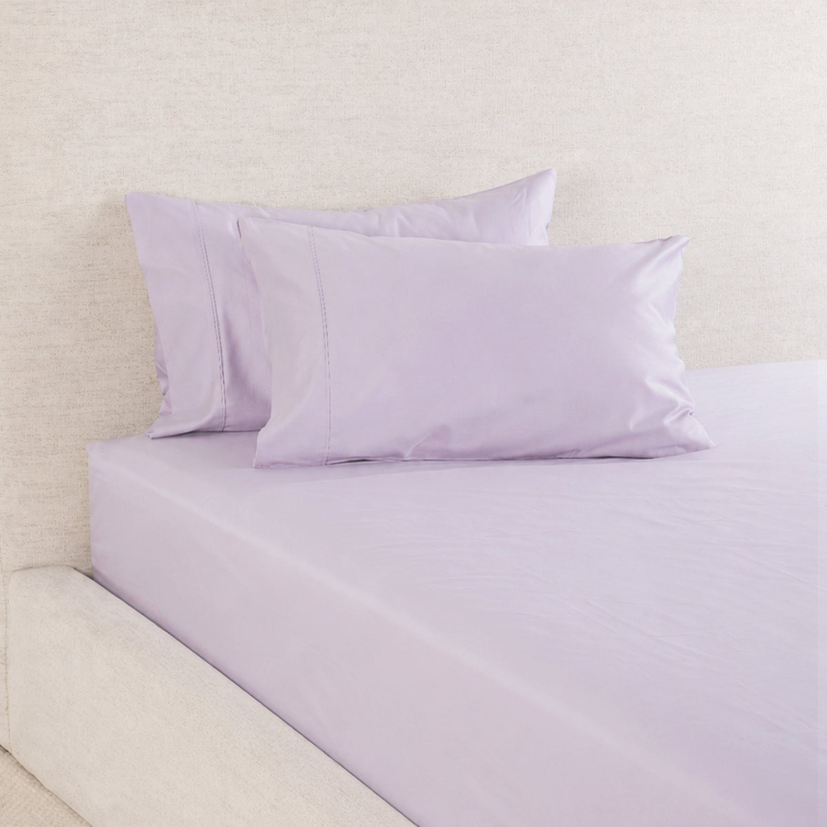 A Gracious Living Avery 750TC 100% Cotton Fitted Sheet in Dusky Mauve, neatly fitted over a mattress and styled with coordinating lavender-purple pillowcases against a neutral upholstered headboard.