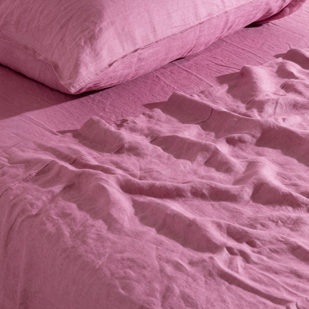 A berry linen flat sheet is softly draped across a bed in natural folds, beautifully highlighting its lightweight woven texture and relaxed, effortless elegance.