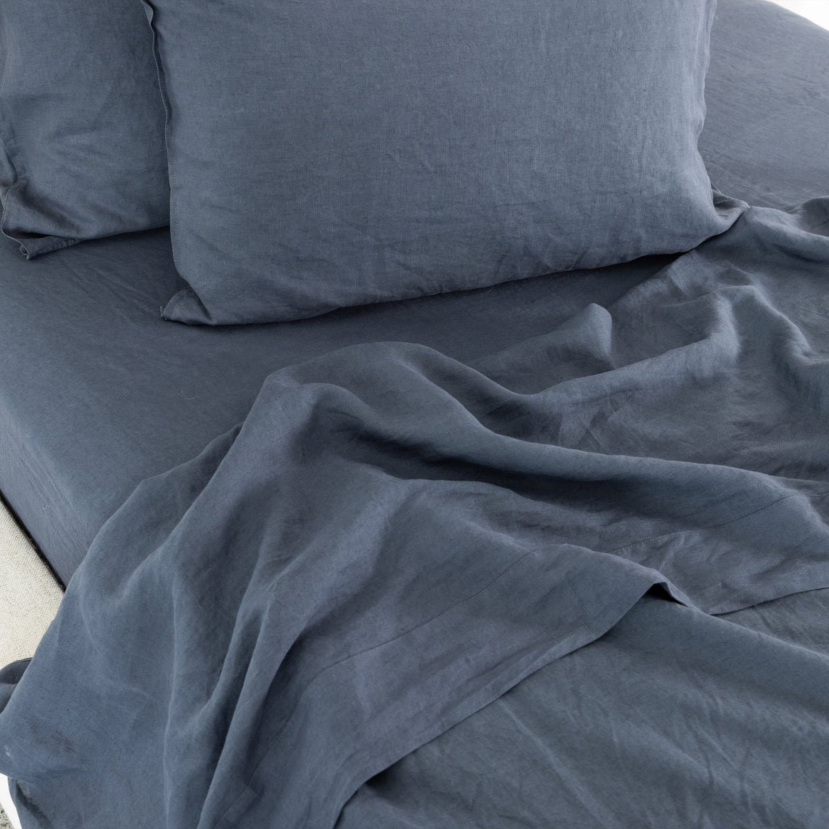 Midnight blue linen bedding is beautifully styled with softly crumpled sheets and plush pillows, showcasing its natural texture and relaxed, lived-in elegance.