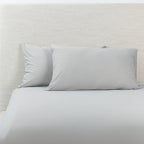 A grey fitted sheet with pillowcases, styled against a textured off-white headboard.