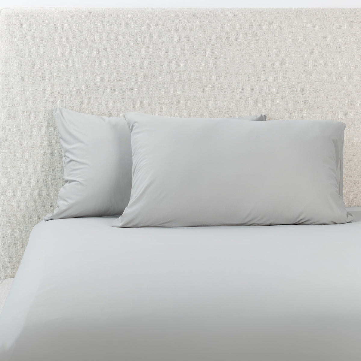 A grey fitted sheet with pillowcases, styled against a textured off-white headboard.