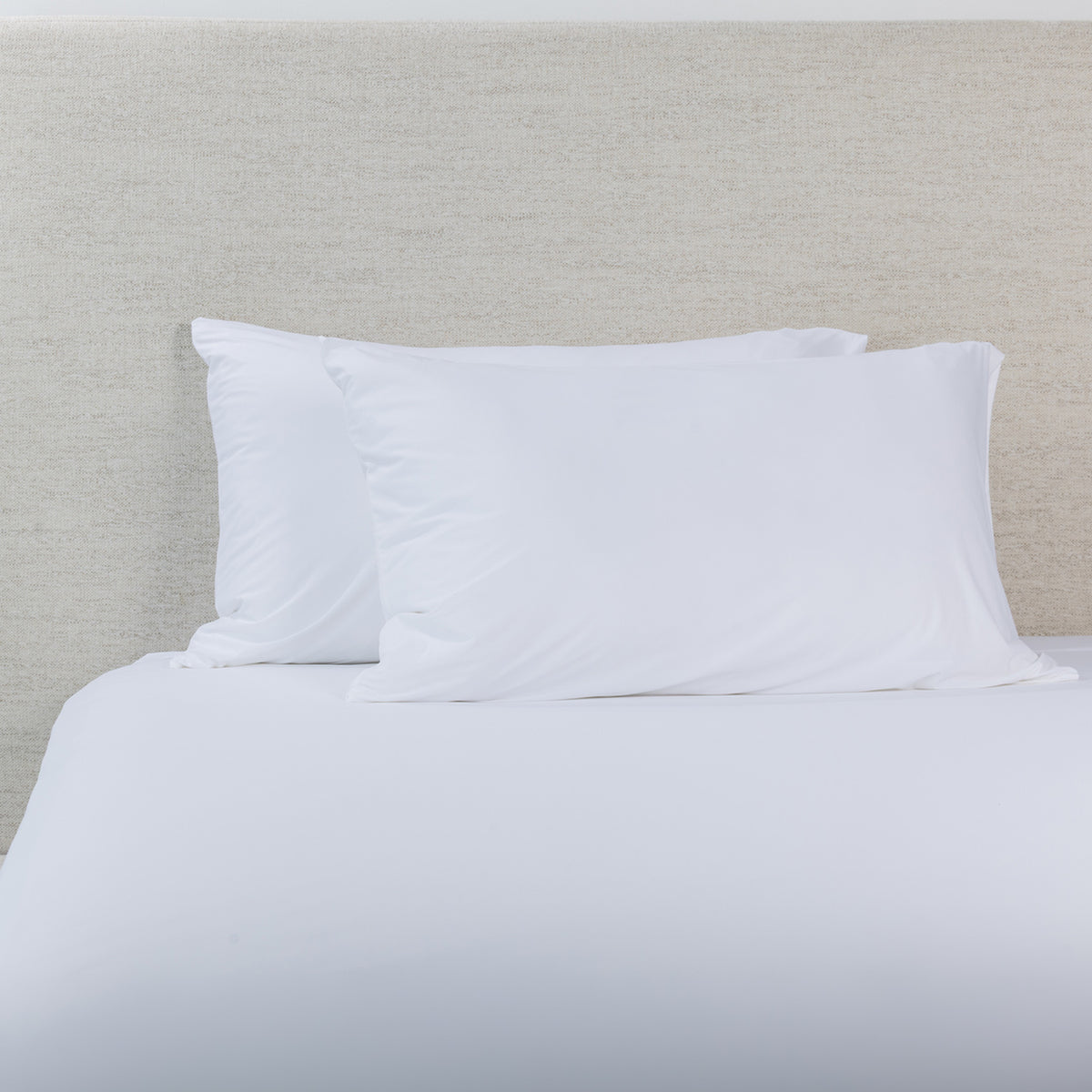 A white fitted sheet with pillowcases, styled against a textured off-white headboard.