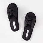 Black sandals with bow details on a white background