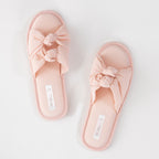 Pair of pink slippers with bow details on a light gray background