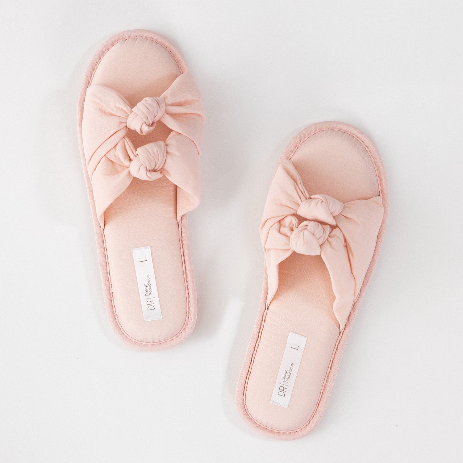 Pair of pink slippers with bow details on a light gray background
