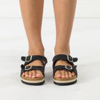 A pair of black woven platform sandals with double straps and silver buckles, shown on a model's feet against a white studio background.