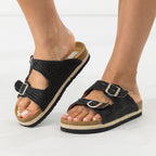 A pair of women's black woven slide sandals with double adjustable straps and silver-tone buckles, shown on a model's feet against a clean white background.