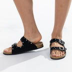 A pair of black double-strap slide sandals with silver buckle closures and stud embellishments, shown on a model's feet against a white background.