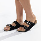 A pair of black double-strap slide sandals with silver buckle closures and stud embellishments, shown on a model's feet against a white background.