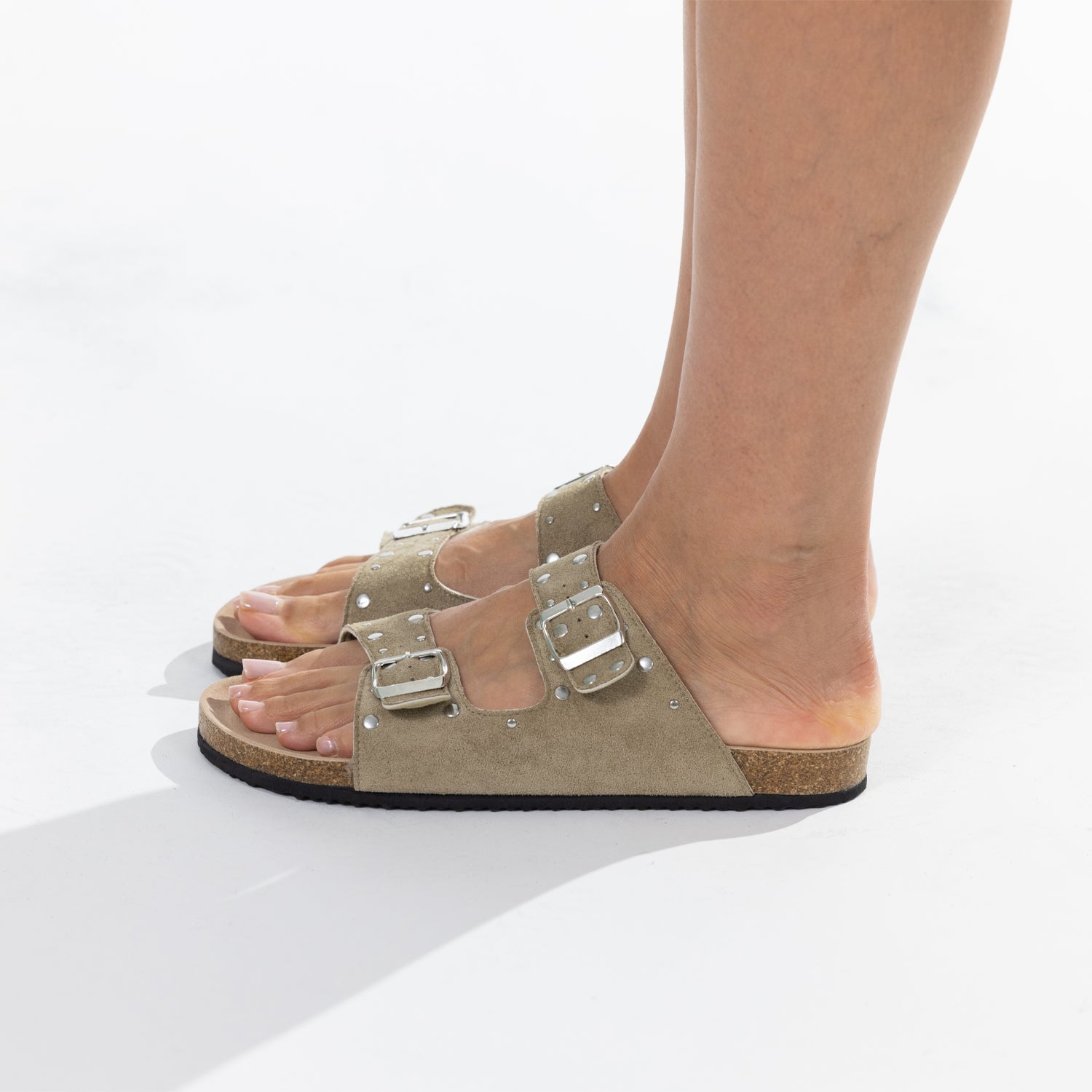 A pair of sage double-strap slide sandals with silver buckle closures and stud embellishments, shown on a model's feet against a white background.