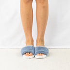 A pair of fluffy chambray blue faux fur slippers is styled on foot, showcasing their plush texture, open-toe design and cosy everyday comfort.