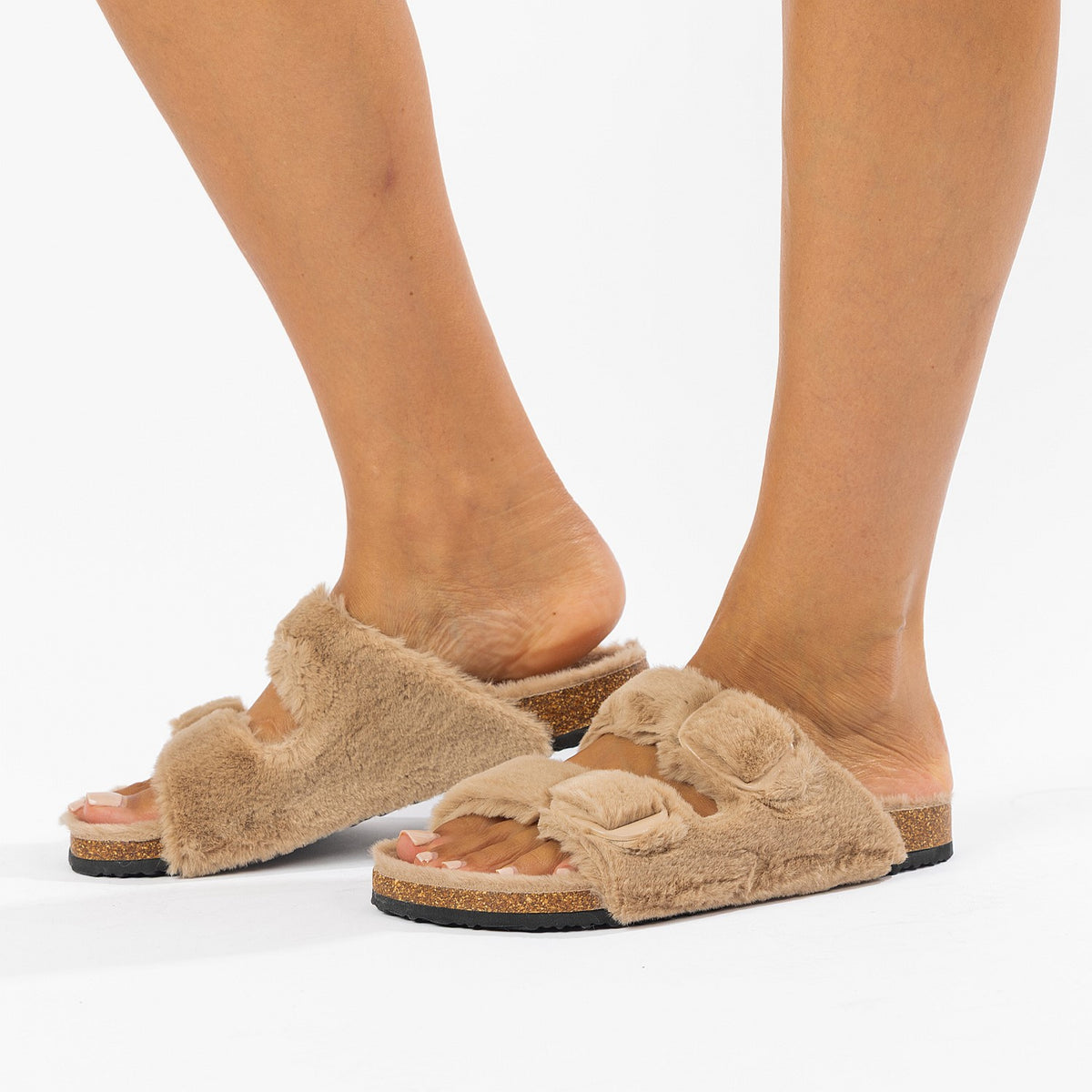 Beige fuzzy slippers worn by a person on a white background