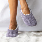 Purple textured slippers worn by a person on a white textured surface