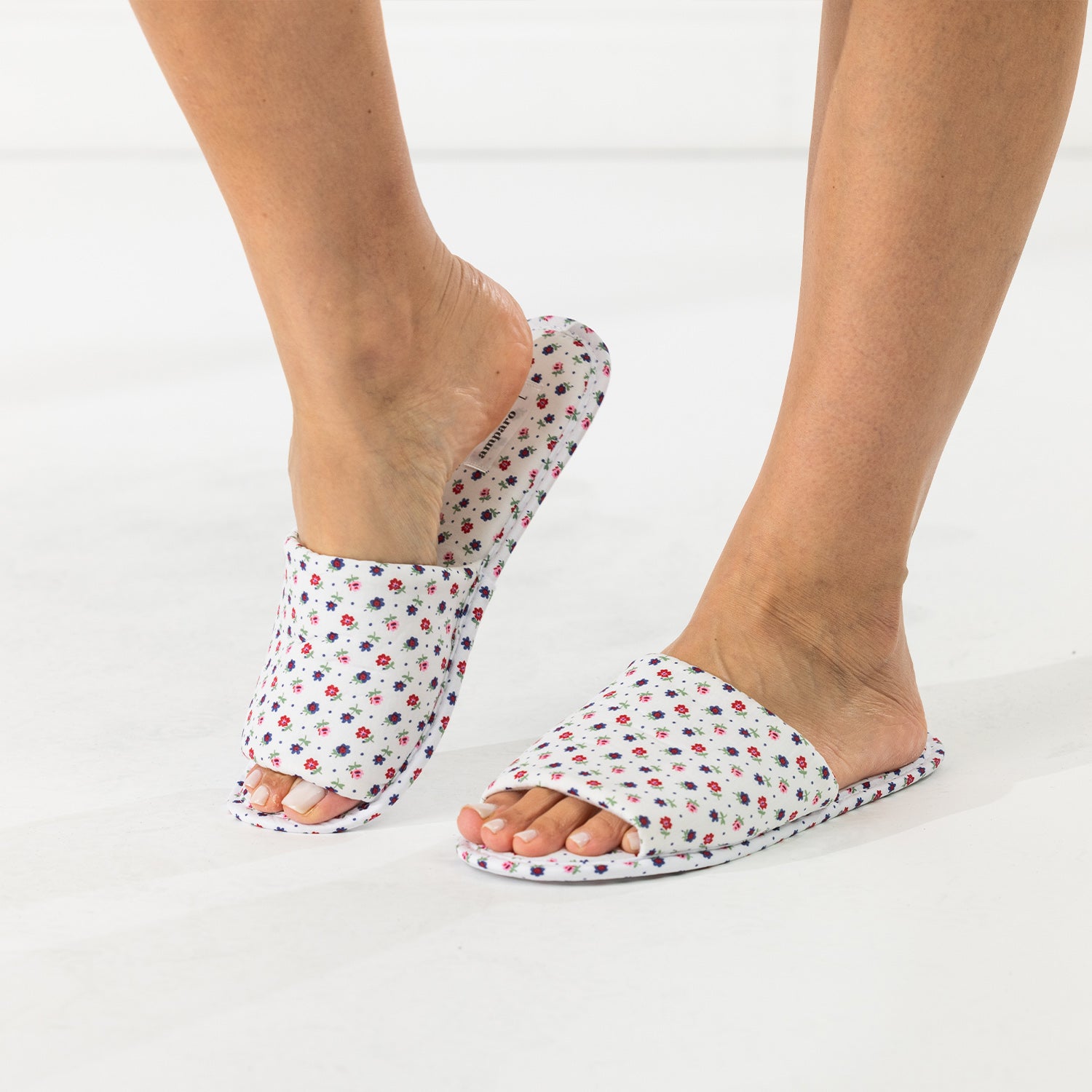 Ivory floral open-toe slippers shown being worn while stepping into one slipper.