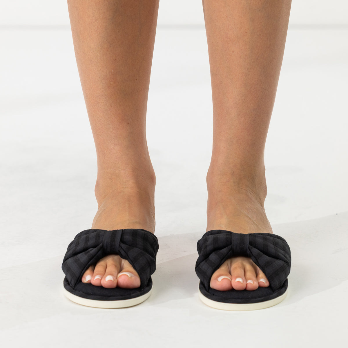Front view of black open-toe slippers with padded crossover straps and bow-inspired detailing.