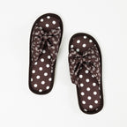 Top view of a pair of chocolate brown open-toe slippers featuring cushioned footbeds with white polka dots, decorative bow-style straps with a white bandana print, and coordinating brown trim on a white background.