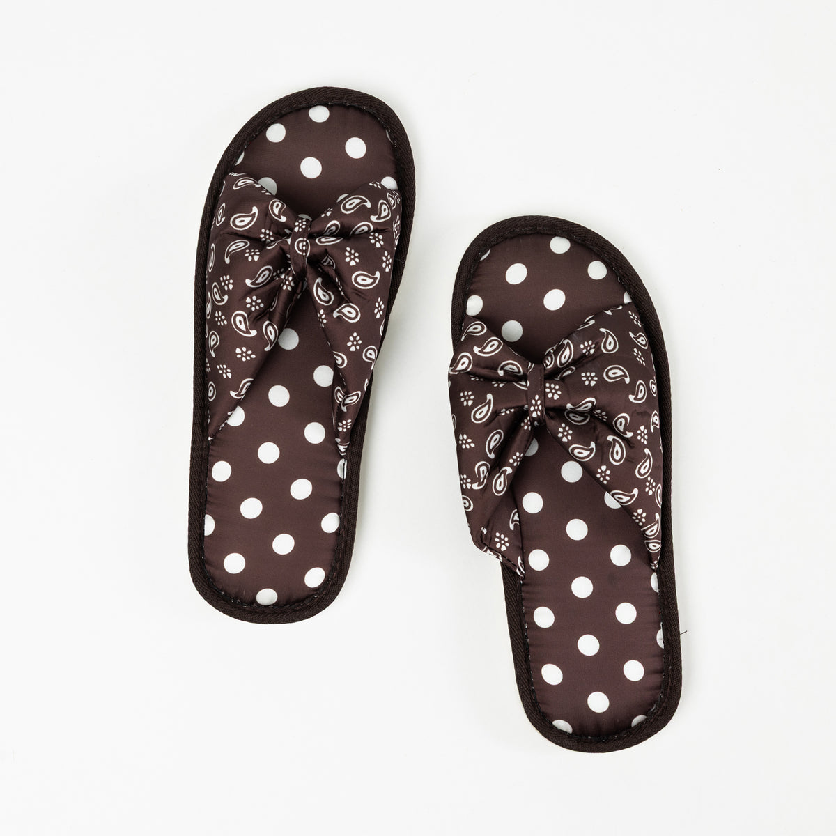Top view of a pair of chocolate brown open-toe slippers featuring cushioned footbeds with white polka dots, decorative bow-style straps with a white bandana print, and coordinating brown trim on a white background.