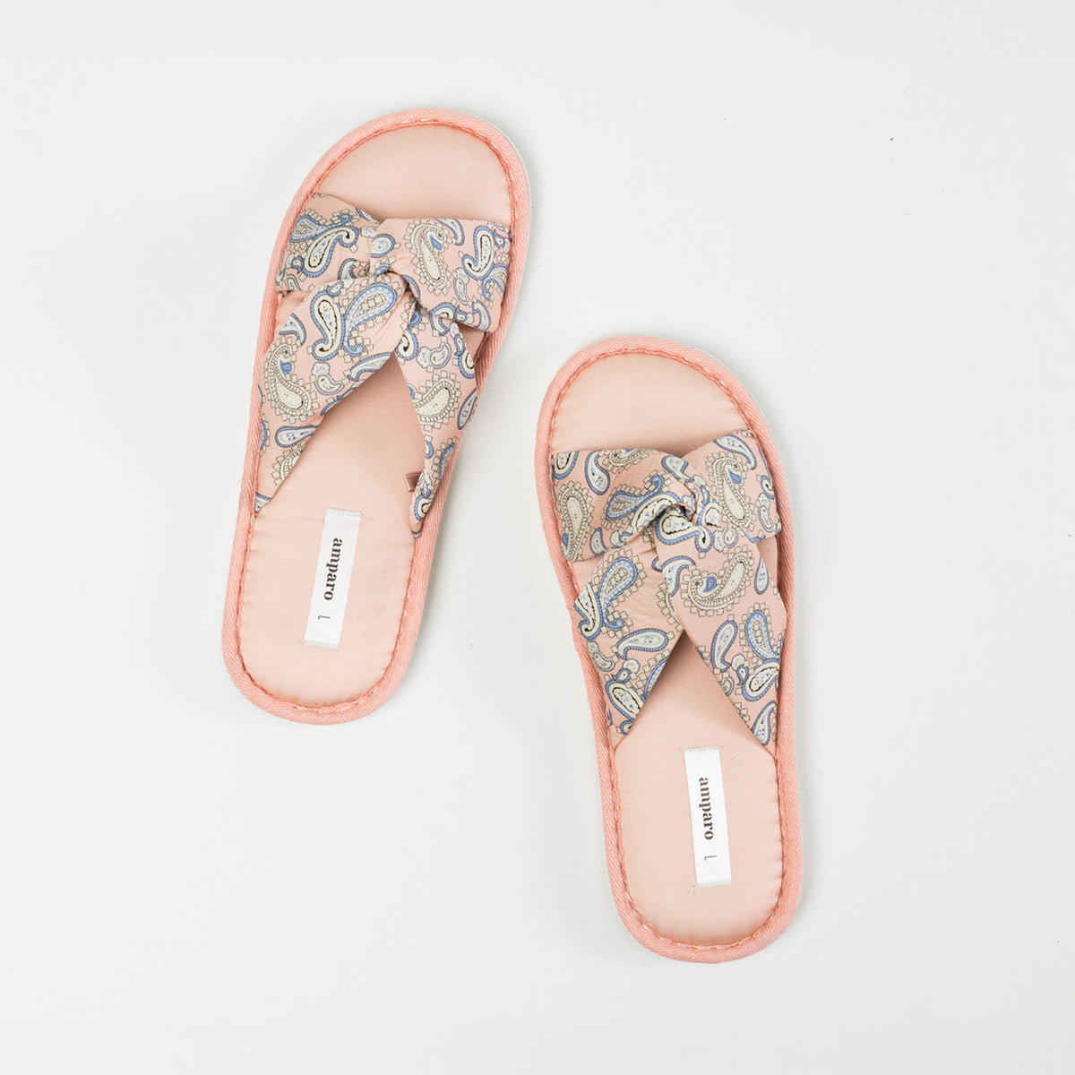 Top view of a pair of pink open-toe slippers featuring cushioned footbeds, crossover straps with a blue and cream paisley bandana print, and coordinating pink trim on a white background.