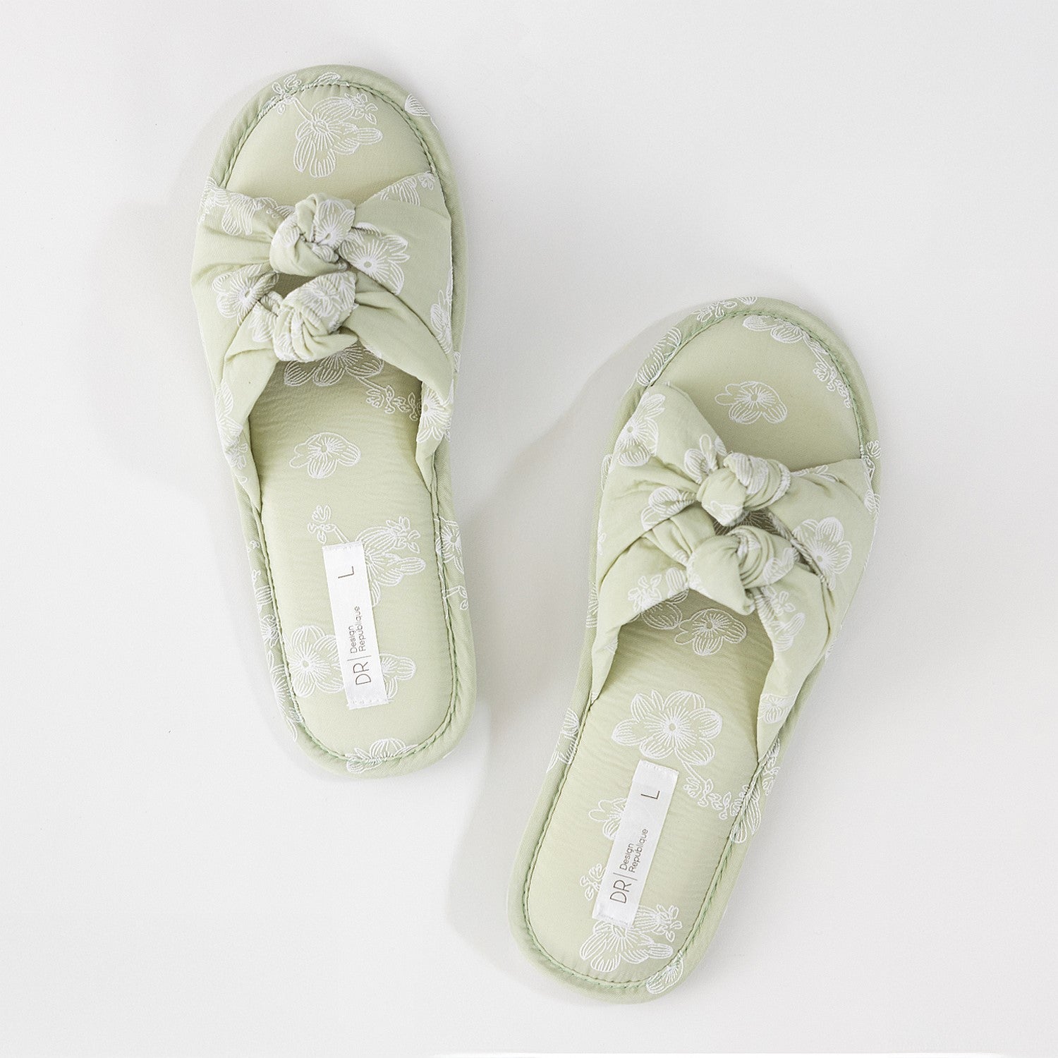 Pair of light green sandals with decorative bows on a white background