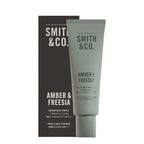 Smith & Co. Amber & Freesia Hand & Nail Pomade 80ml in a sage green tube displayed alongside its black packaging against a white background.