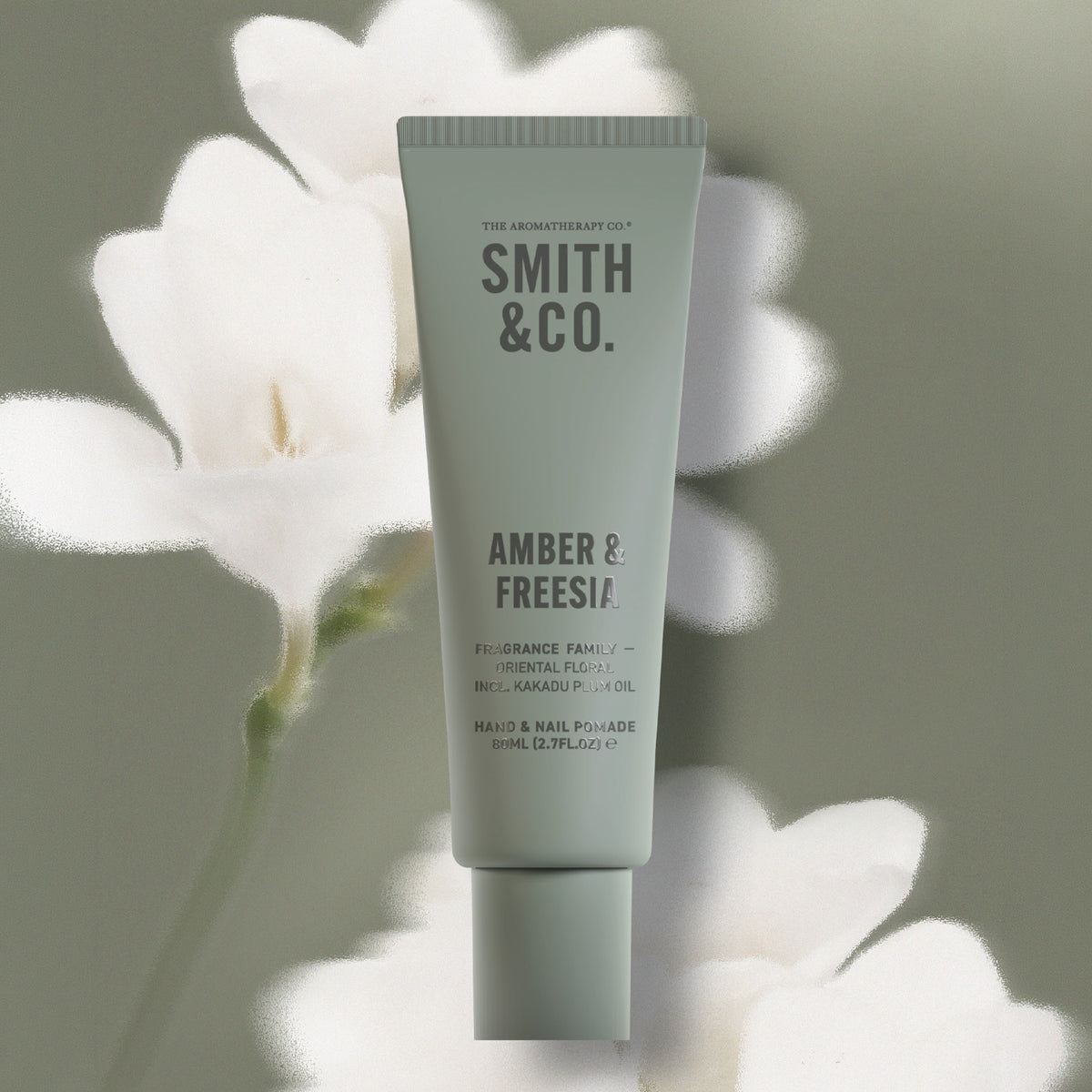 Smith & Co. Amber & Freesia Hand & Nail Pomade 80ml in a sage green tube against a soft floral background with white flowers.