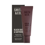 Smith & Co. Black Oud & Saffron Hand & Nail Pomade 80ml in a burgundy tube displayed alongside its black packaging against a white background.
