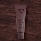 Smith & Co. Black Oud & Saffron Hand & Nail Pomade 80ml in a burgundy tube against a dark burgundy woodgrain background.