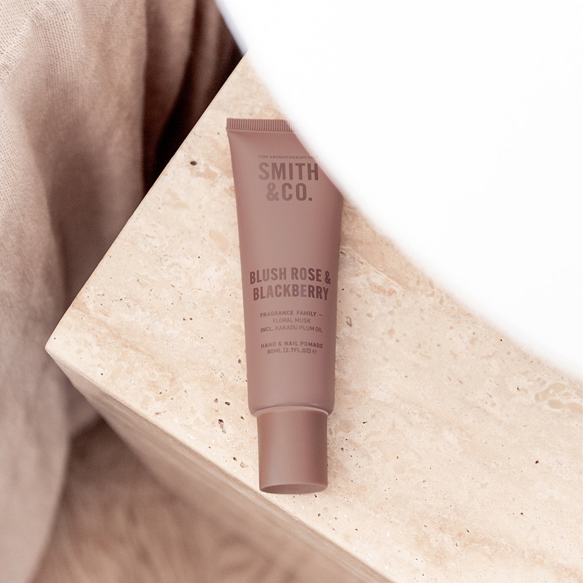 Smith & Co. Blush Rose & Blackberry Hand & Nail Pomade 80ml resting on a beige stone surface beside soft neutral fabric.