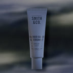 Smith & Co. Smoked Suede & Bergamot Hand & Nail Pomade 80ml in a dusty blue tube against a softly blurred dark background.
