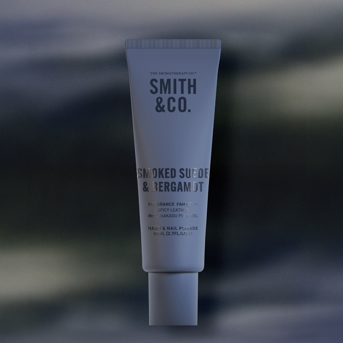 Smith & Co. Smoked Suede & Bergamot Hand & Nail Pomade 80ml in a dusty blue tube against a softly blurred dark background.
