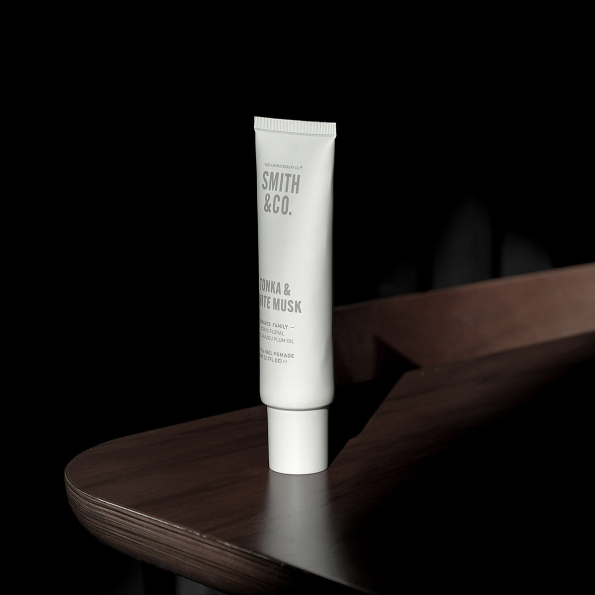 A white squeeze tube of Smith & Co. Hair & Skin Rescue Mask & Treat, labeled 'OMRA & WHITE MASK', standing on a dark wooden surface against a solid black background.