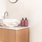 Two Smith & Co. Blush Rose & Blackberry pink pump bottles displayed beside a textured stone basin on a marble bathroom countertop.