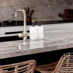Two Smith & Co. Tonka & White Musk white pump bottles displayed beside a brushed brass tap on a marble kitchen island with woven bar stools.