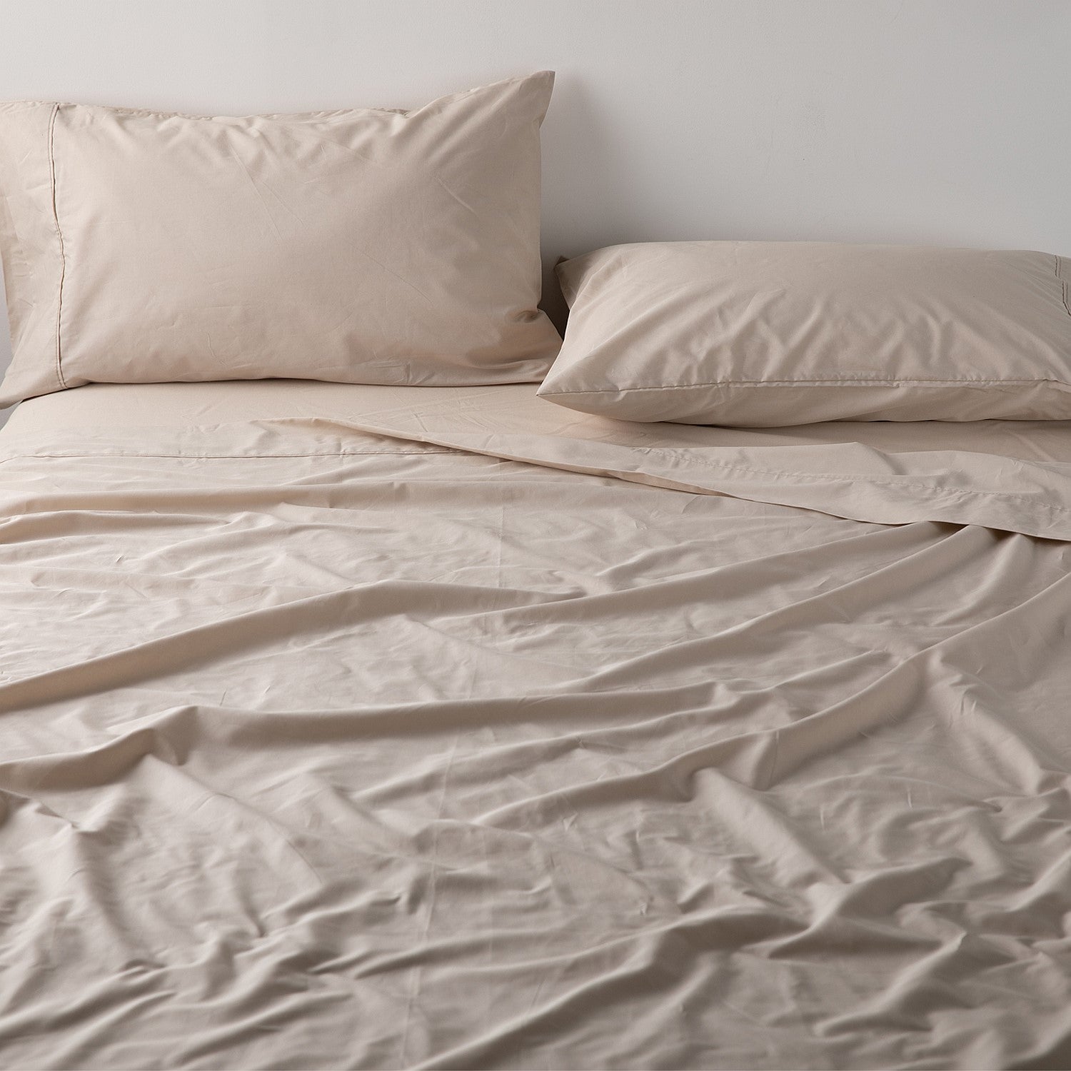 Beige bedding set with two pillows on a bed against a plain wall.