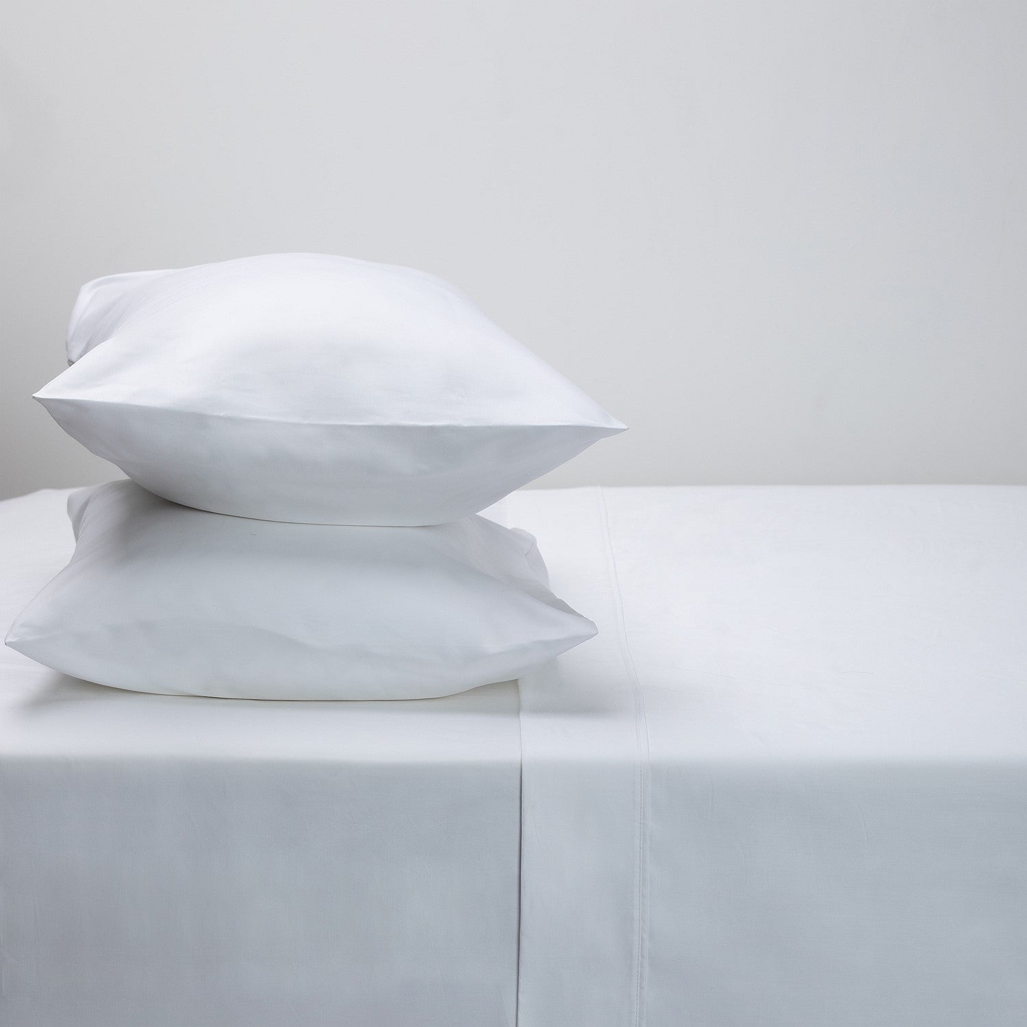Two white pillows on a white bed sheet with a plain background