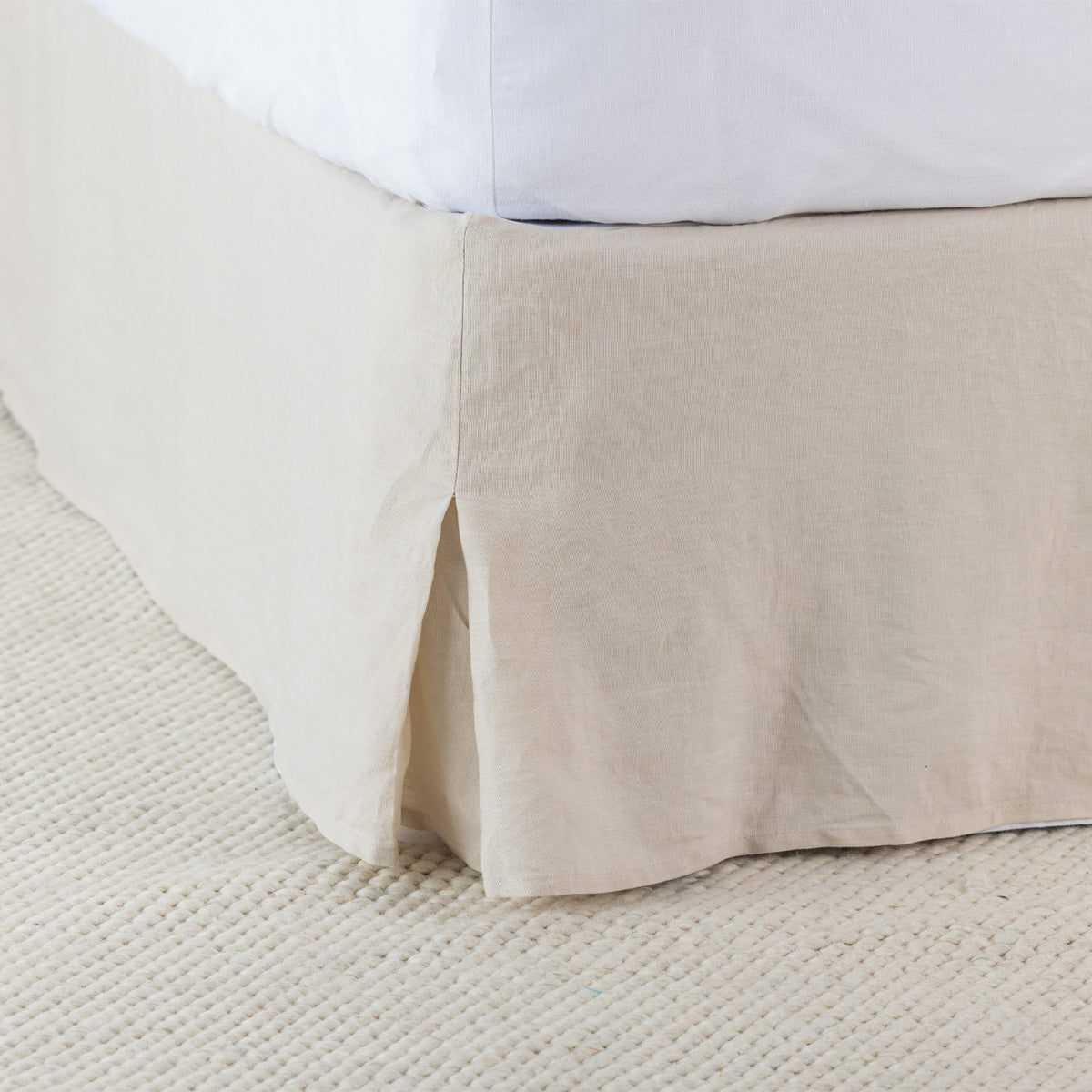 A natural beige linen valance drapes elegantly around the base of a bed, showcasing its soft woven texture, tailored finish and relaxed, timeless appeal.