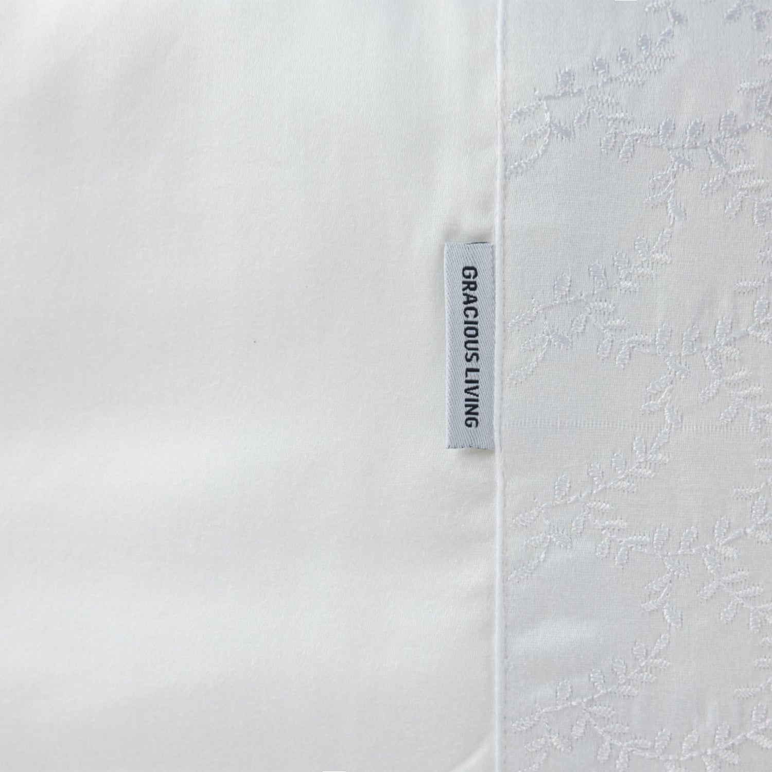 Close up of the Gracious Living Celine Embroidery Sheet Set in White, showing the embroidered leaf cuff and brand label.