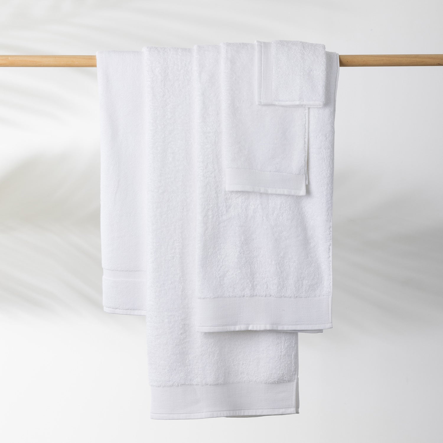 White Egyptian cotton towel collection including a bath sheet, bath towel and hand towel hanging on a wooden towel rail.