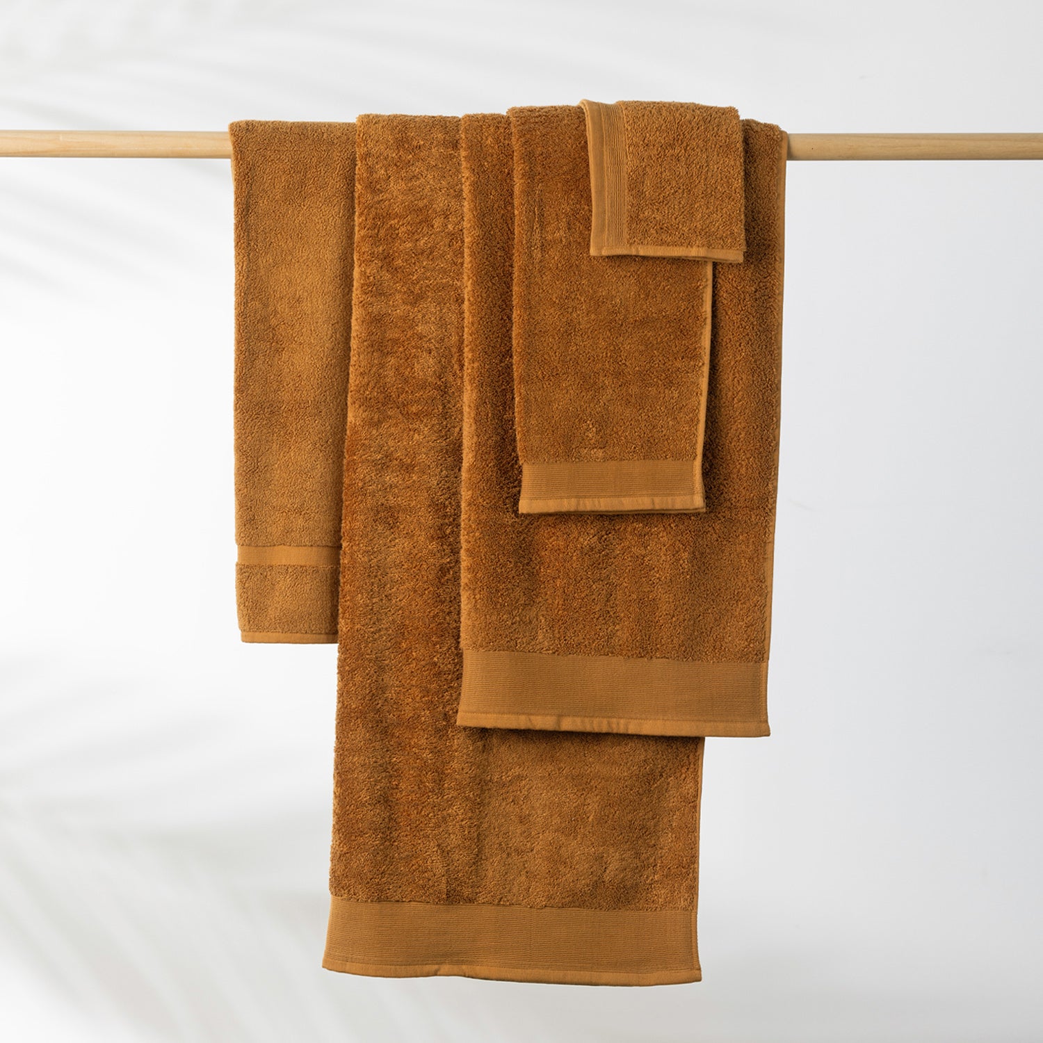 Marigold Egyptian cotton towel collection including a bath sheet, bath towel and hand towel hanging on a wooden towel rail.