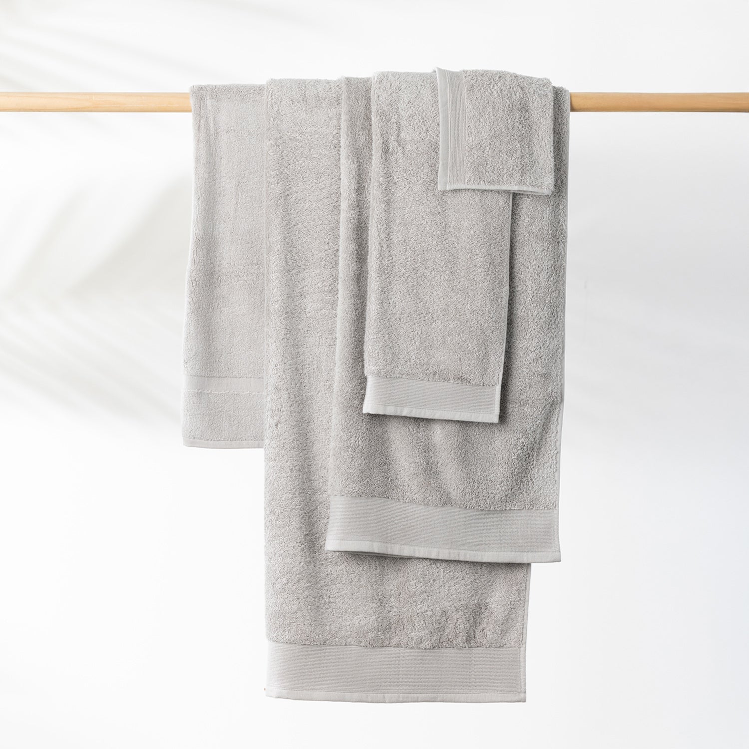 Silver Egyptian cotton towel collection including a bath sheet, bath towel and hand towel hanging on a wooden towel rail.