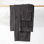 Charcoal Egyptian cotton towel collection including bath towel, hand towel and face cloth neatly displayed hanging over a wooden towel rail.